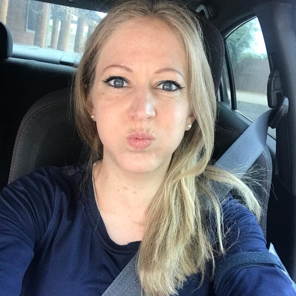 blonde woman with puckered lips taking a selfie from the front seat of her car