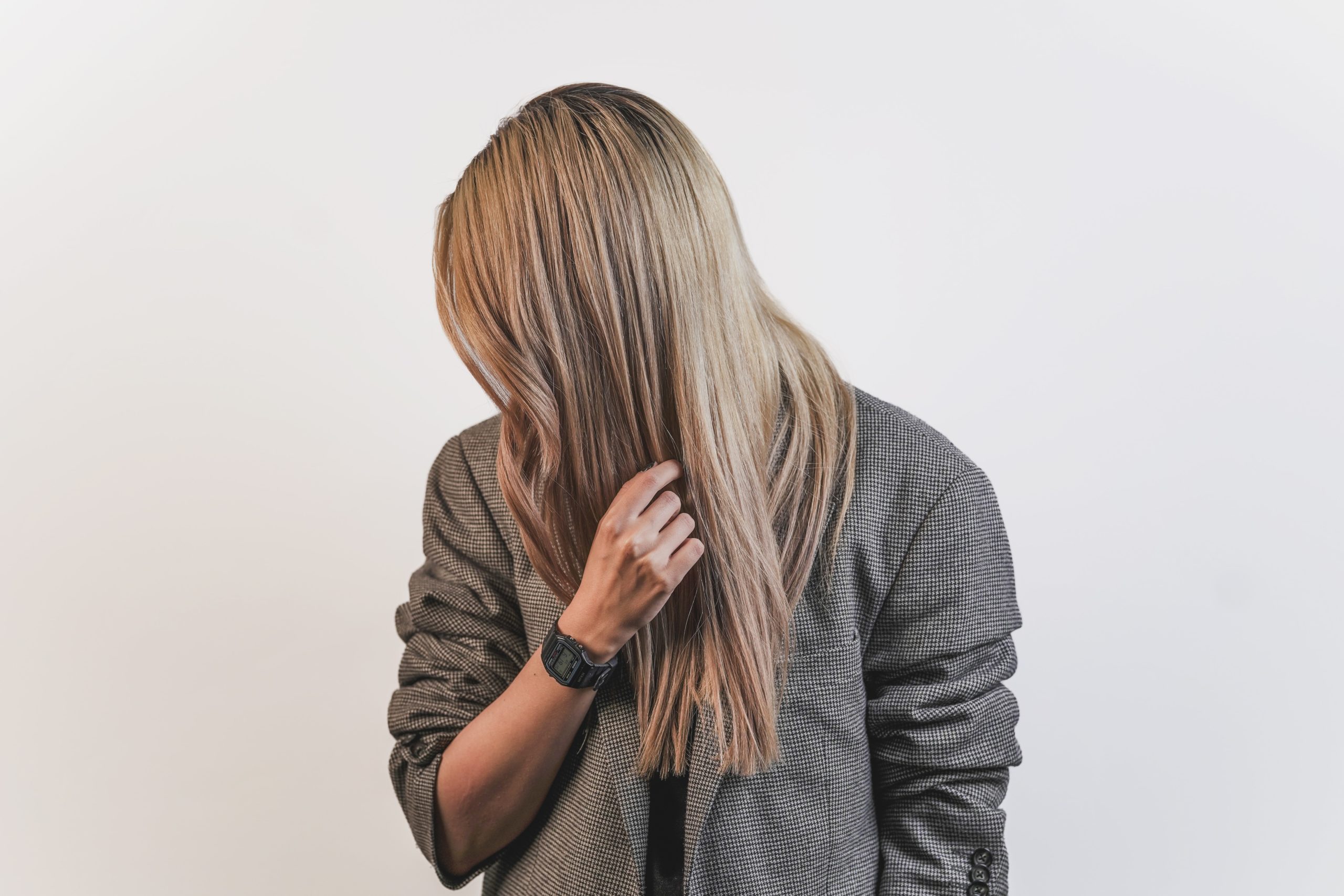 woman with a watch on in front of a white background hiding her face with her hair